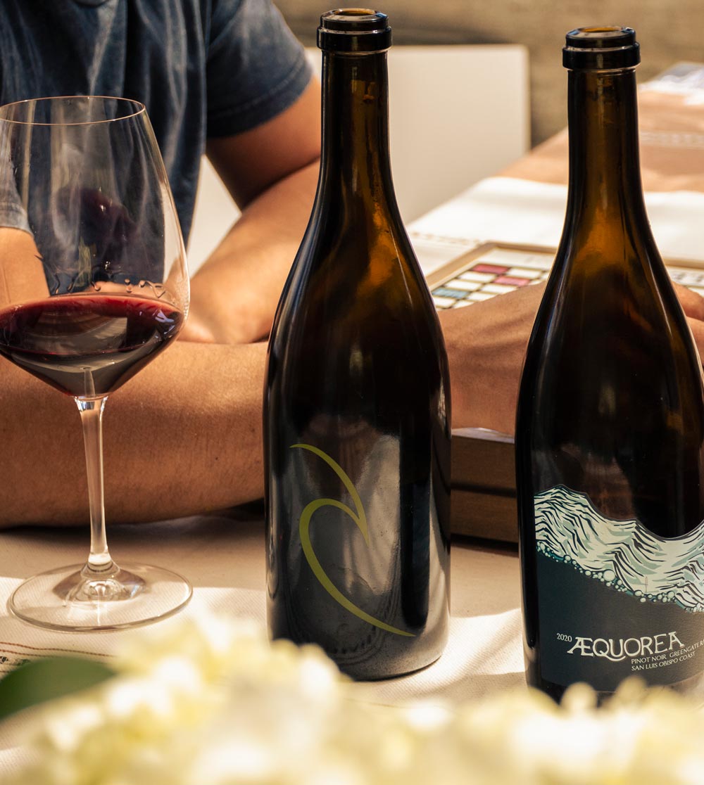 Glass of wine next to Aaron and Aequorea wine bottles